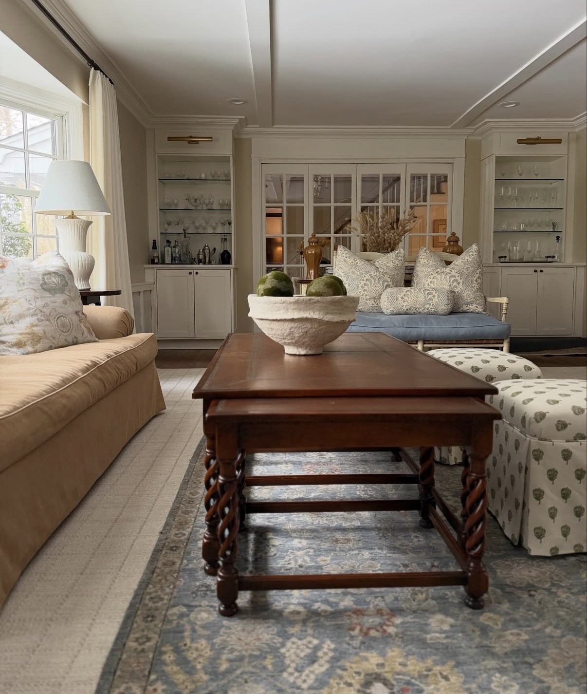 Family room with built-in cabinetry, a long wood coffee table and upholstered ottomans